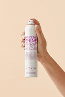 Hand holding a can of 'Make Me Shine Spray Gloss' by Eleven on a beige background - Hair Care Canada