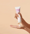 Hand holding a tube of 'Frizz Control Shaping Cream' with visible brand name on a beige background - Hair Care Canada