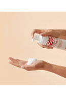 Person holding a bottle of 'I Want Body Volume Foam' with foam on palm against a beige background - Hair Care Canada