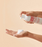 Person holding a bottle of 'I Want Body Volume Foam' with foam on palm against a beige background - Hair Care Canada