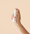 Hand holding a white spray bottle with red text against a beige background - Hair Care Canada