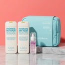 A hair care gift set by Elvin's featuring two white bottles of shampoo and conditioner, a small pink bottle of leave-in conditioner, and a light blue zippered pouch, arranged on a white marble block against a solid coral-pink background.