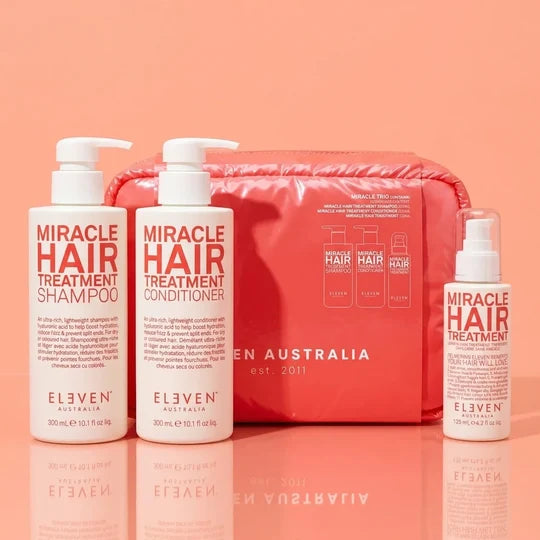 Eleven Australia Miracle Hair Treatment set including shampoo, conditioner, and a small spray bottle, displayed in front of a red zippered pouch on a peach background.