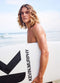 Man holding a surfboard with 'Kevin Murphy' branding on a beach Hair Care Canada