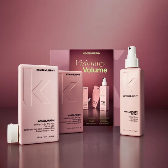 Kevin Murphy Visionary Volume hair care set featuring a pink Angel Wash bottle, Angel Rinse bottle, and Antigravity Spray bottle, alongside a product box, arranged on a reflective surface against a matching pink background.