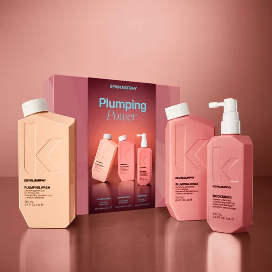 Kevin Murphy Plumping Power hair care set featuring a peach-colored shampoo bottle, a pink conditioner bottle, a pink body mass bottle, and the product box on a matching pink background.