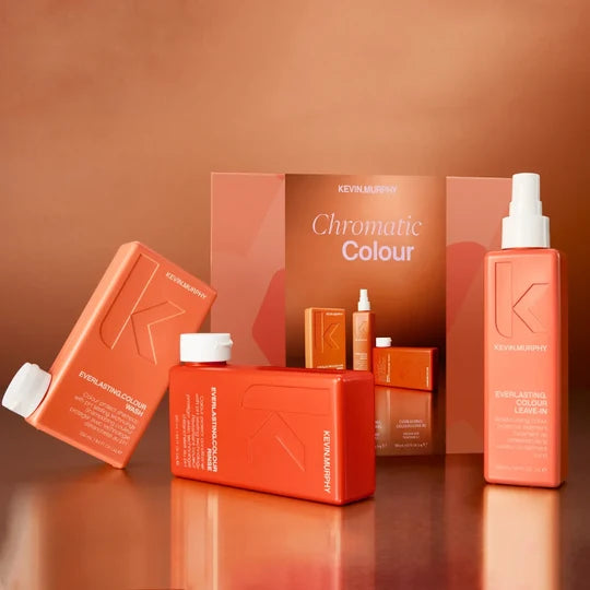 Kevin Murphy Chromatic Colour hair color product set with multiple bottles and boxes in a warm copper-orange color scheme, arranged on a reflective surface with a matching backdrop.