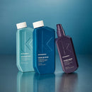 Three Kevin Murphy haircare bottles on a reflective blue surface against a blue gradient background: a light aqua Repair Me Wash bottle, a medium blue Repair Me Rinse bottle, and a dark purple Young Again spray bottle.