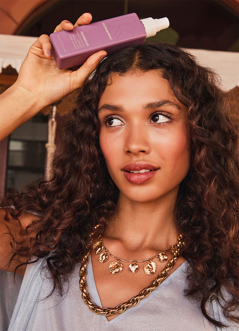 Woman applying purple shampoo to her hair with a neutral background - Hair Care Canada