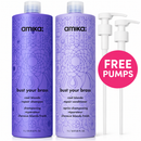 Two Amika 'Bust Your Brass' cool blonde repair shampoo and conditioner bottles in purple, shown alongside two white pump bottles and a pink circular badge that reads 'FREE PUMPS'.