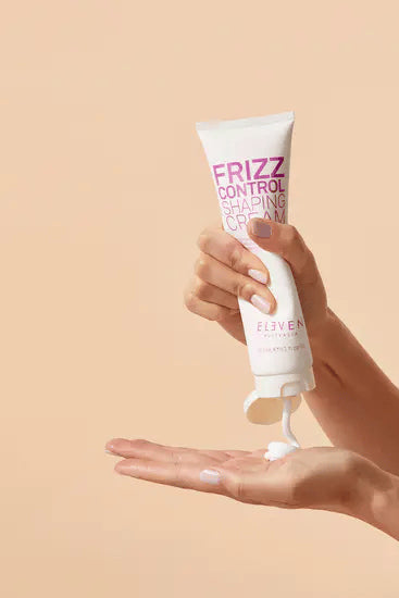 Hand holding a tube of 'Frizz Control Shaping Cream' with visible brand name on a beige background - Hair Care Canada