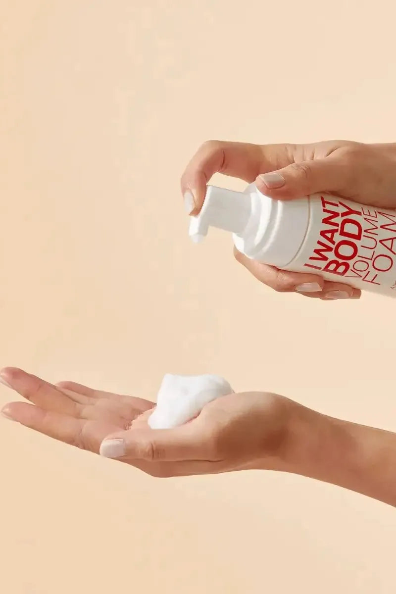 Person holding a bottle of 'Want Body' volume foam with a beige background - Hair Care Canada