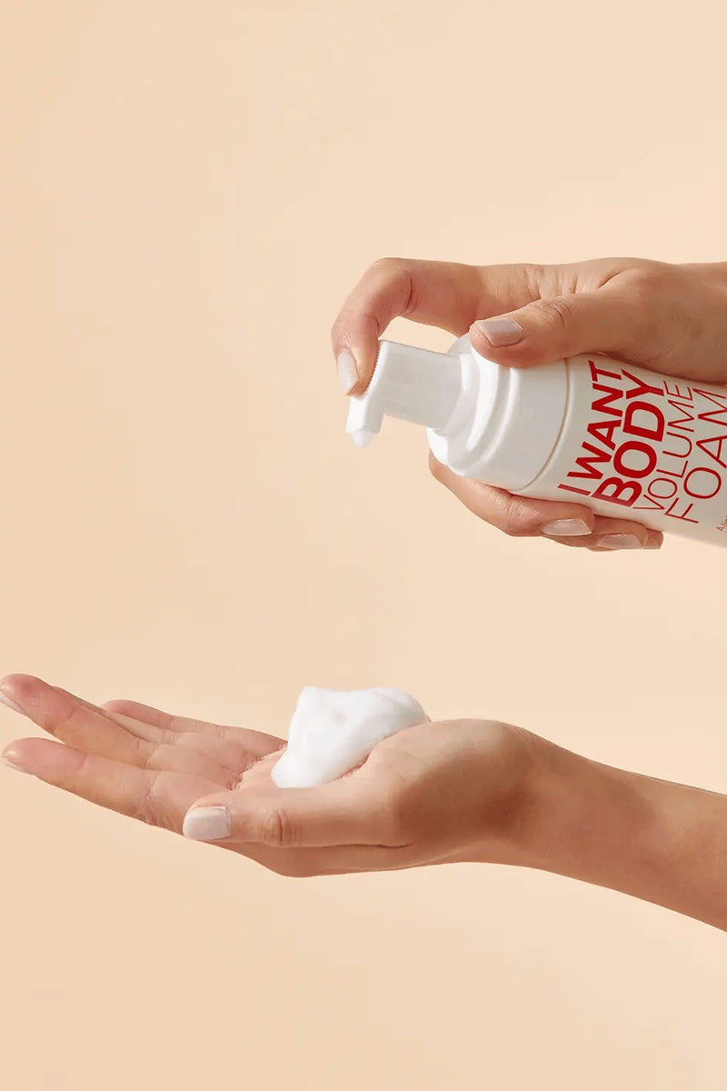 Person holding a bottle of 'Want Body' volume foam with a beige background - Hair Care Canada