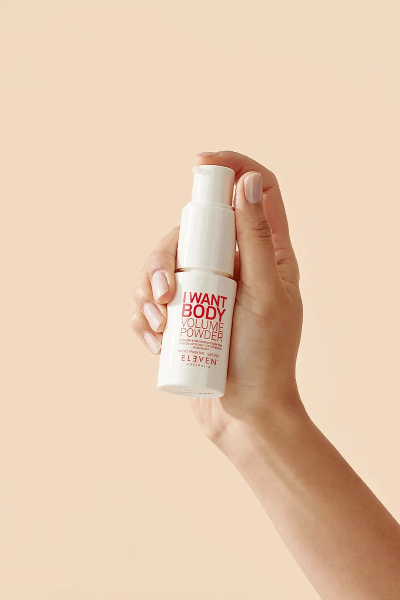 Hand holding a white spray bottle with red text against a beige background - Hair Care Canada