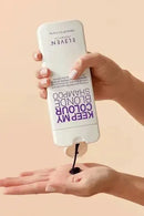 Hand holding a bottle of Eleven Shampoo and Conditioner with product being poured into another hand on a beige background - Hair Care Canada