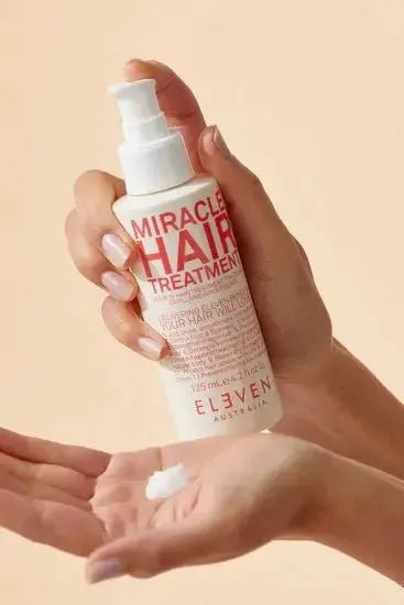 Hand holding a bottle of 'Miracle Hair Treatment' by Eleven Australia against a beige background - Hair Care Canada