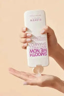 Hand holding a bottle of shampoo with visible text on a beige background - Hair Care Canada