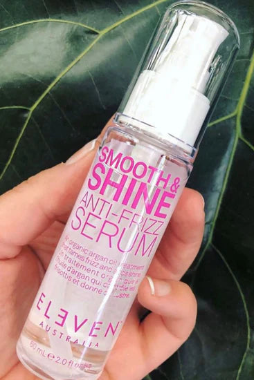 Hand holding a bottle of 'Smooth & Shine Anti-Frizz Serum' by Eleven Australia against a leafy background Hair Care Canada