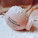 Kevin Murphy Volumizing Powder in a pale pink bottle tipped on its side, covered with white powder, on a surface scattered with loose powder.