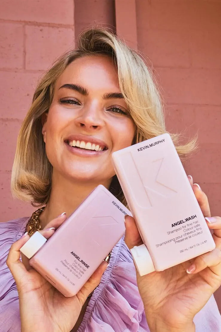 Woman holding Kevin Murphy hair products against a pink brick wall - Hair Care Canada