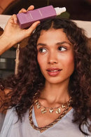 Woman applying purple shampoo to her hair with a neutral background - Hair Care Canada