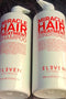 Two bottles of Eleven Australia Miracle Hair Treatment Shampoo and Conditioner on a textured surface Hair Care Canada